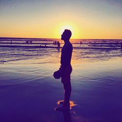 Silhouette man standing on beach against sky during sunset