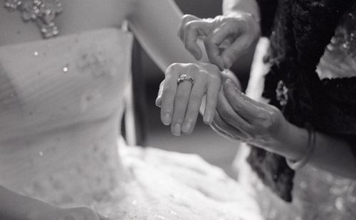 Cropped hands of bridesmaid tying thread on bride hand c during wedding