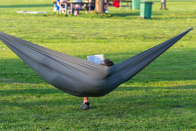 Man reading book in comfortable hammock at green garden on warm spring evening, viev from behind