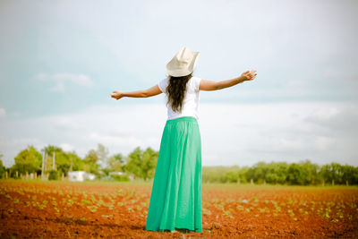 Rear view of woman wearing hat standing on field against sky