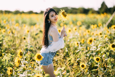 Portrait of young woman standing amidst flowering plants on field