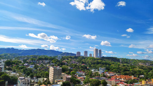 Trees and buildings against cloudy sky