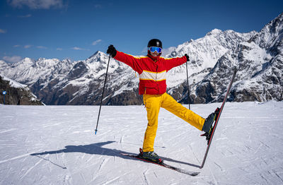 Young man with ski makes pose in mountains behind