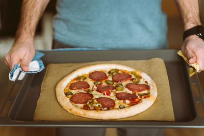 A man holds a baking sheet with pizza. baking sheet covered with baking paper