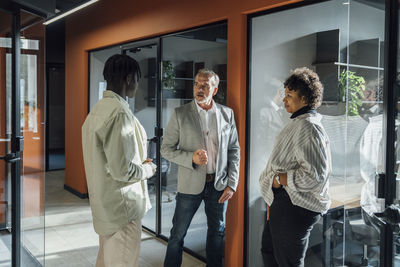 Mature businessman discussing with colleagues standing by glass