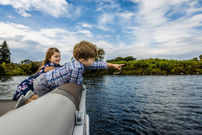 Boy pointing while enjoying with sister in boat on lake against sky