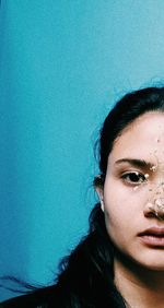 Close-up portrait of young woman against blue wall