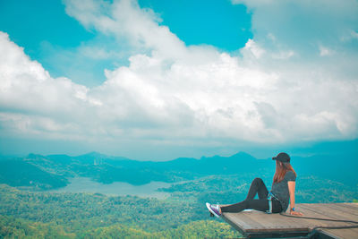 Side view of woman looking at mountains while sitting on observation point