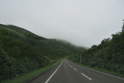 Empty road along trees and mountains against sky