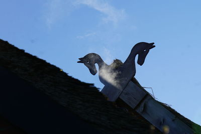 Low angle view of bird sculpture on roof against sky