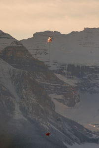 Person hanging from air vehicle against mountain during sunset