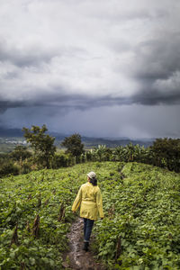 Young woman wearing yellow coat walks through lush field in guatemala.