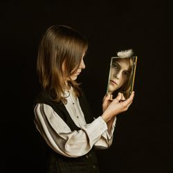 Side view of young woman using mobile phone against black background