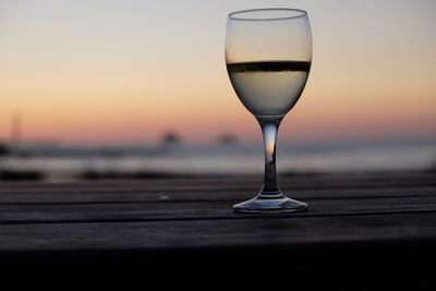 Close-up of wineglass against sea during sunset
