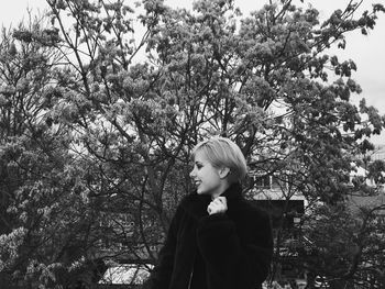 Smiling young woman looking away while sitting against tree in park