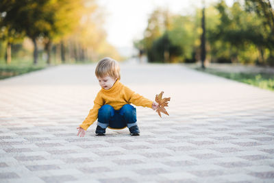 Full length of boy sitting on footpath