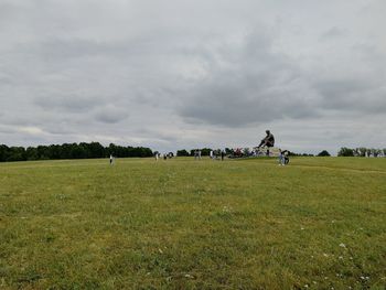 People on grassy field against cloudy sky at park