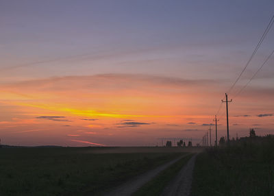 Road passing through field at sunset