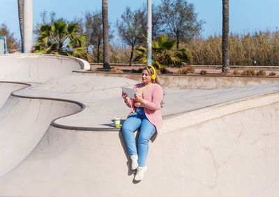 Full length of young woman sitting in skateboard park