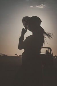 Side view of man photographing against sky during sunset