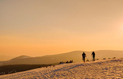 People walking on snow covered land against sky during sunset