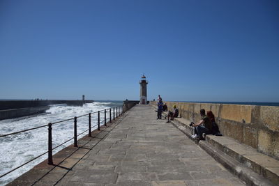 People sitting on promenade by sea against clear sky