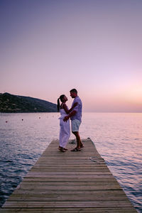 Rear view of couple walking on sea against sky during sunset