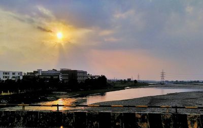 Buildings by river against sky during sunset