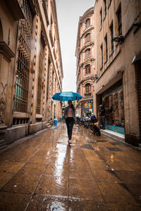 Rear view of man walking on wet street during rainy season