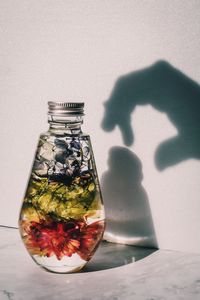 Reflection of person in glass jar on table against wall