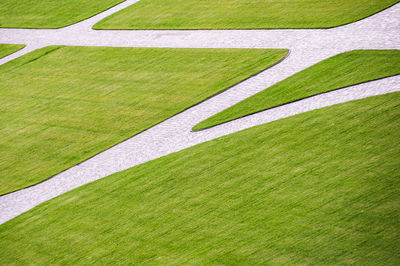 Cobbled park alleys and a wooden park bench. all surrounded by green grass on a sunny, bright day. 