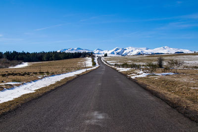 Road leading towards snowcapped mountain against blue sky