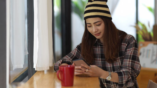 Young woman using mobile phone while sitting on table