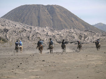 People riding horses on landscape against mountains