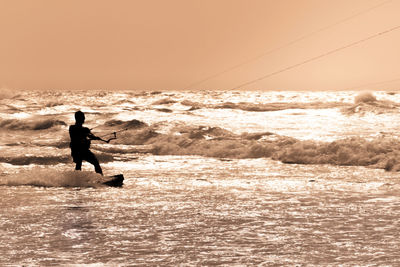 Silhouette man surfing in sea against sky