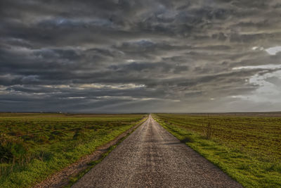 Road passing through agricultural field against sky