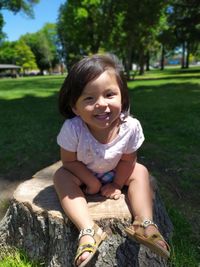 Portrait of smiling baby girl sitting on tree stump in park