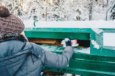 Rear view of woman putting garbage in can during winter