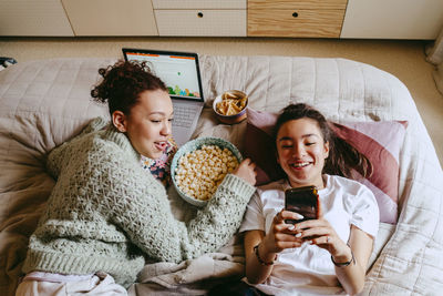 Happy female friends with smart phone and laptop spending leisure time at home