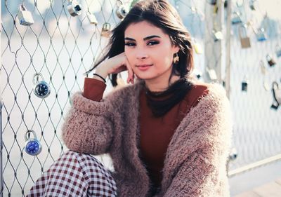 Portrait of beautiful young woman sitting by fence