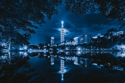 Illuminated buildings by lake against sky at night