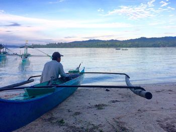 Man sitting on boat moored at sea shore against sky