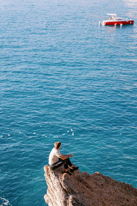 High angle view of man sitting on rock by sea