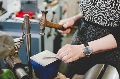 Midsection of senior woman hammering on metal to make jewelry in workshop