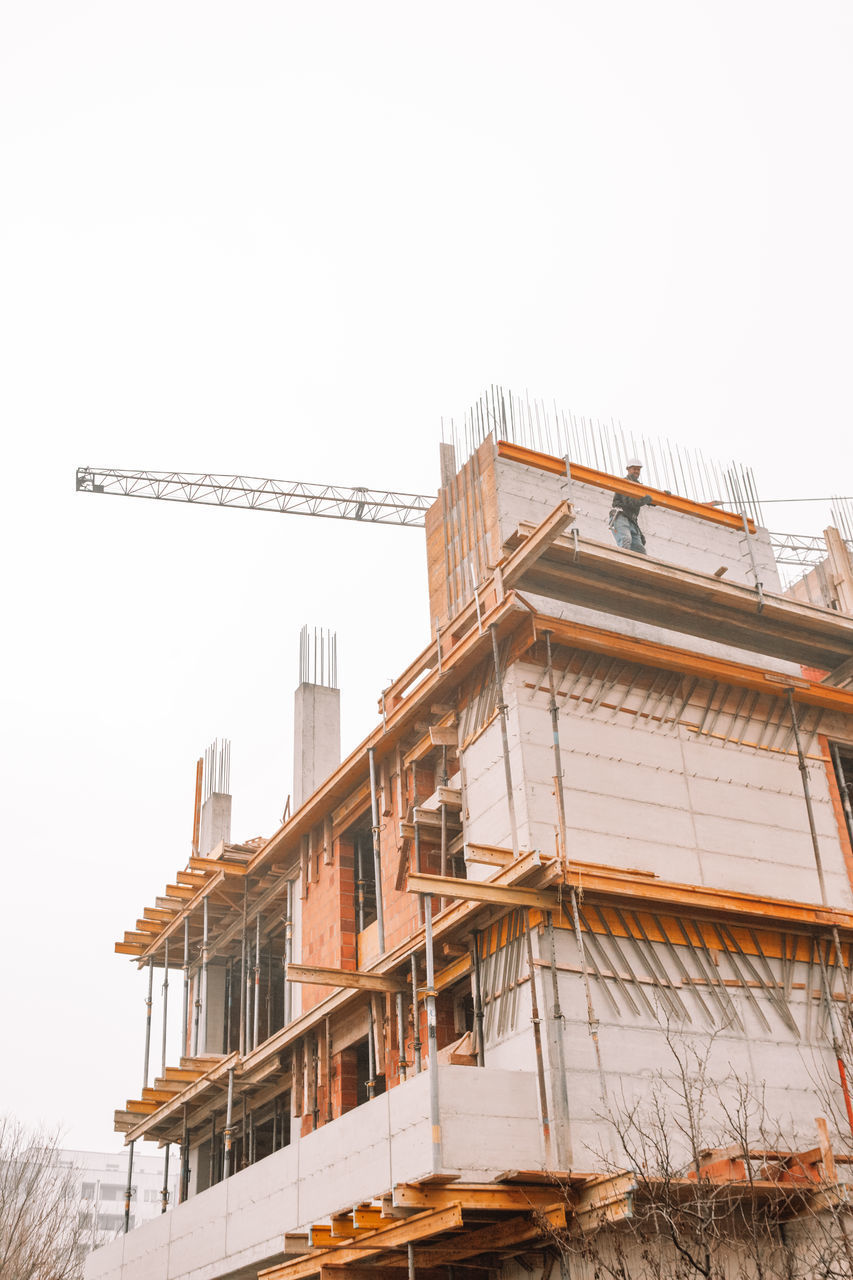 LOW ANGLE VIEW OF CRANE BY BUILDING AGAINST SKY