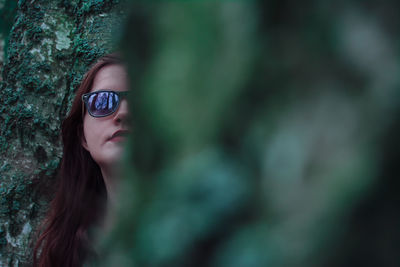 Woman wearing sunglasses against mossy wall