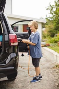 Full length side view of girl charging electric car on driveway