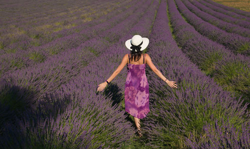 Rear view of woman standing on field with purple flowers