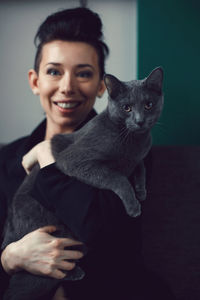 Portrait of smiling young woman with cat against black background