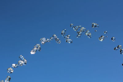 Low angle view of water flying against clear blue sky